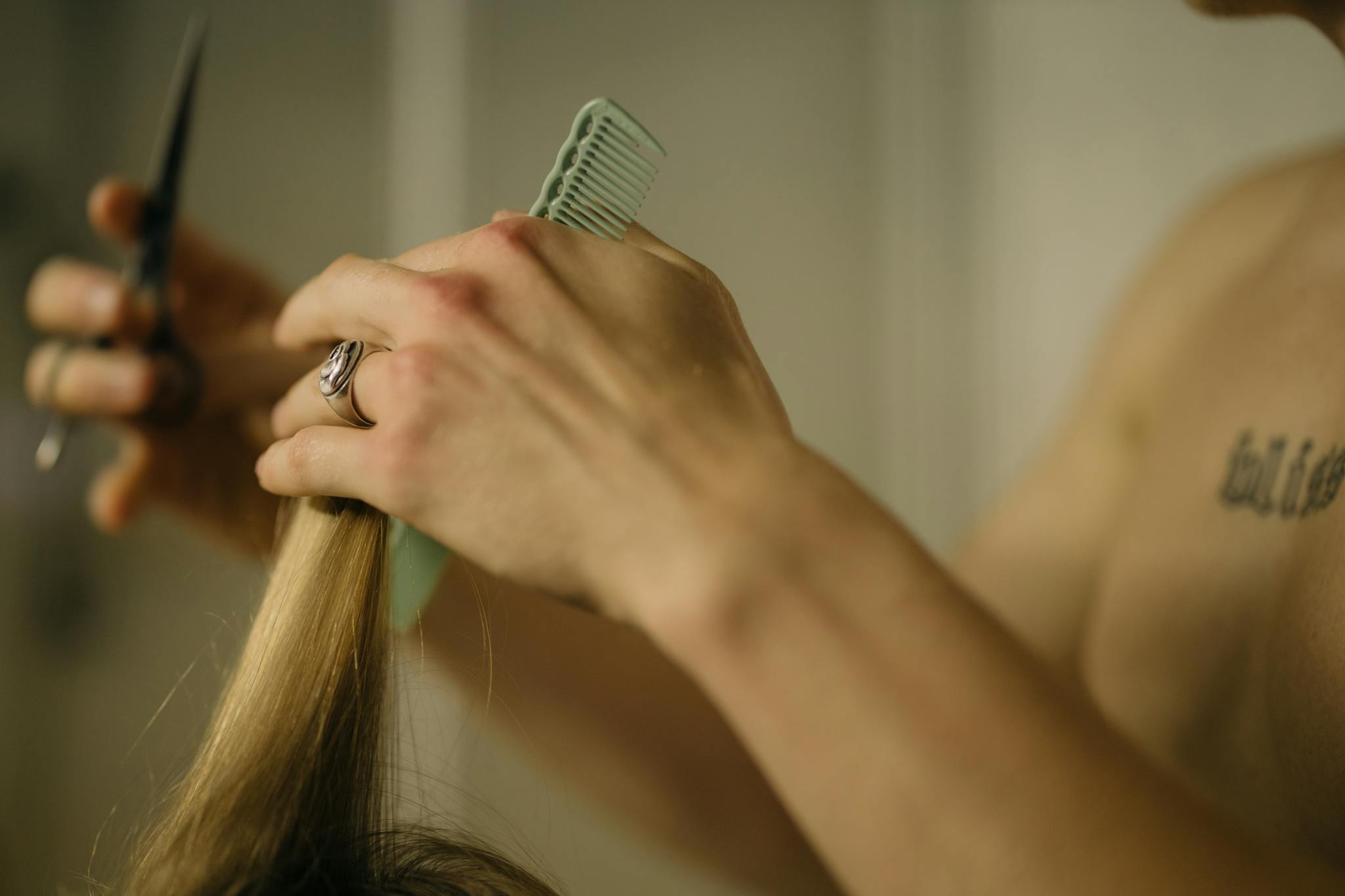 Hairdresser using scissors and comb for a haircut. Detailed close-up of hands brushing blonde hair.